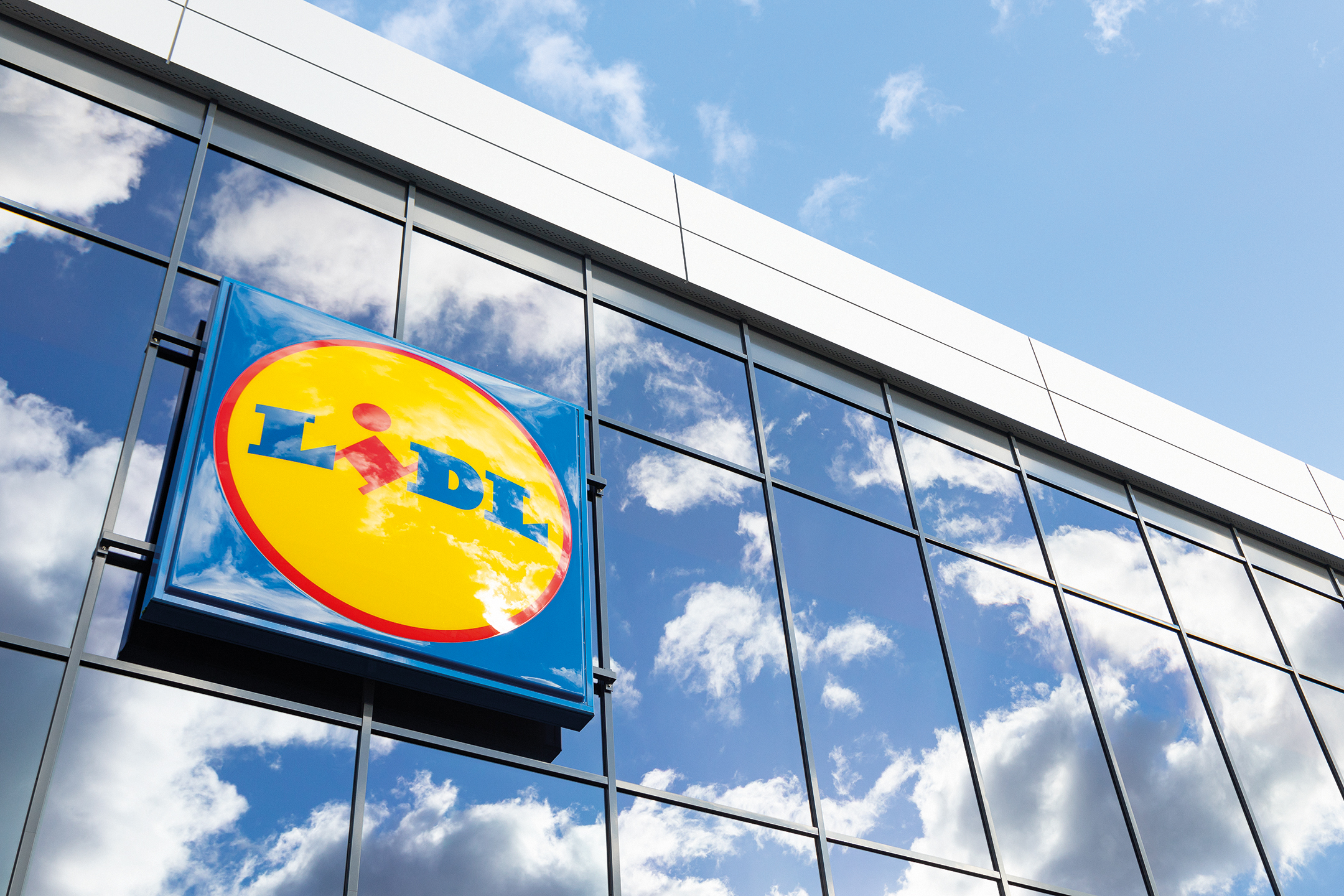 Letreiro do Lidl numa fachada de vidro com reflexo do céu e nuvens.