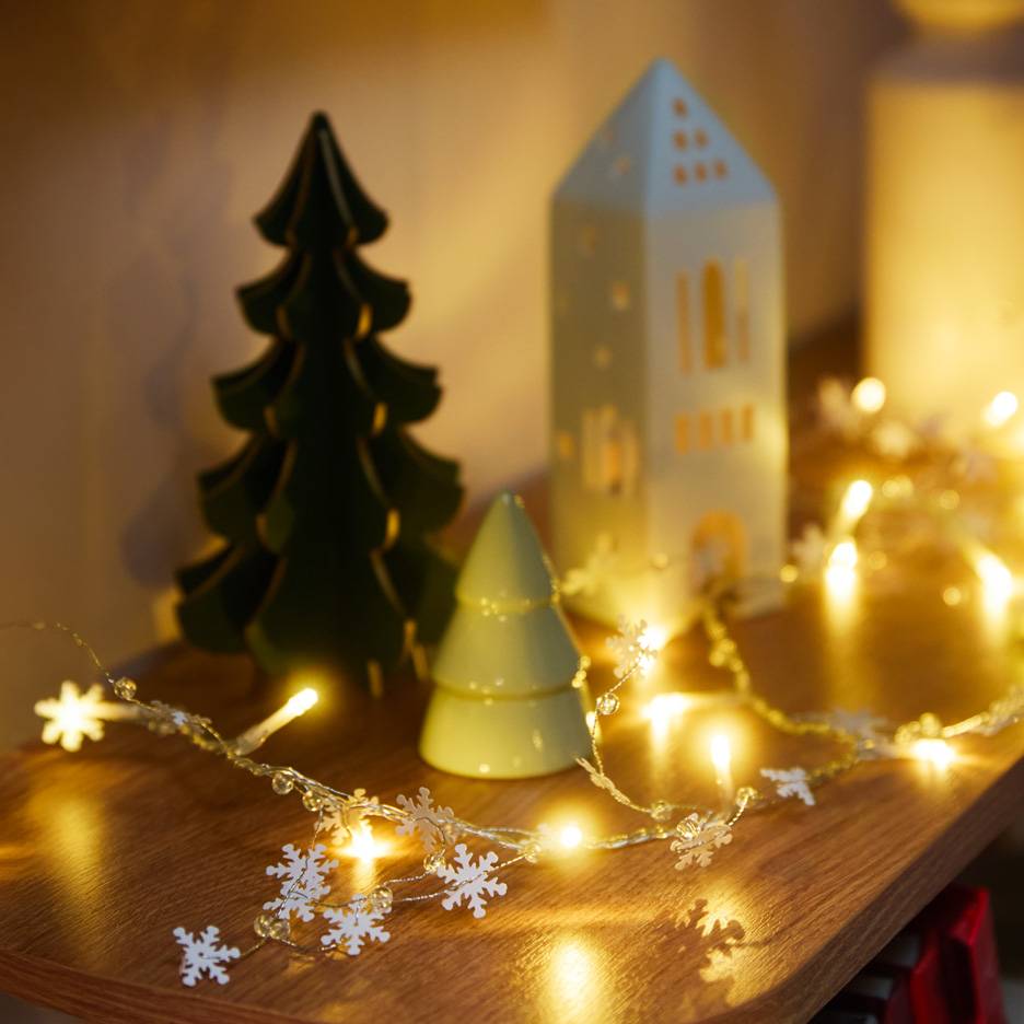 Decorações de Natal: uma árvore verde escura, uma árvore verde clara, uma casa branca e um fio de luzes de floco de neve.