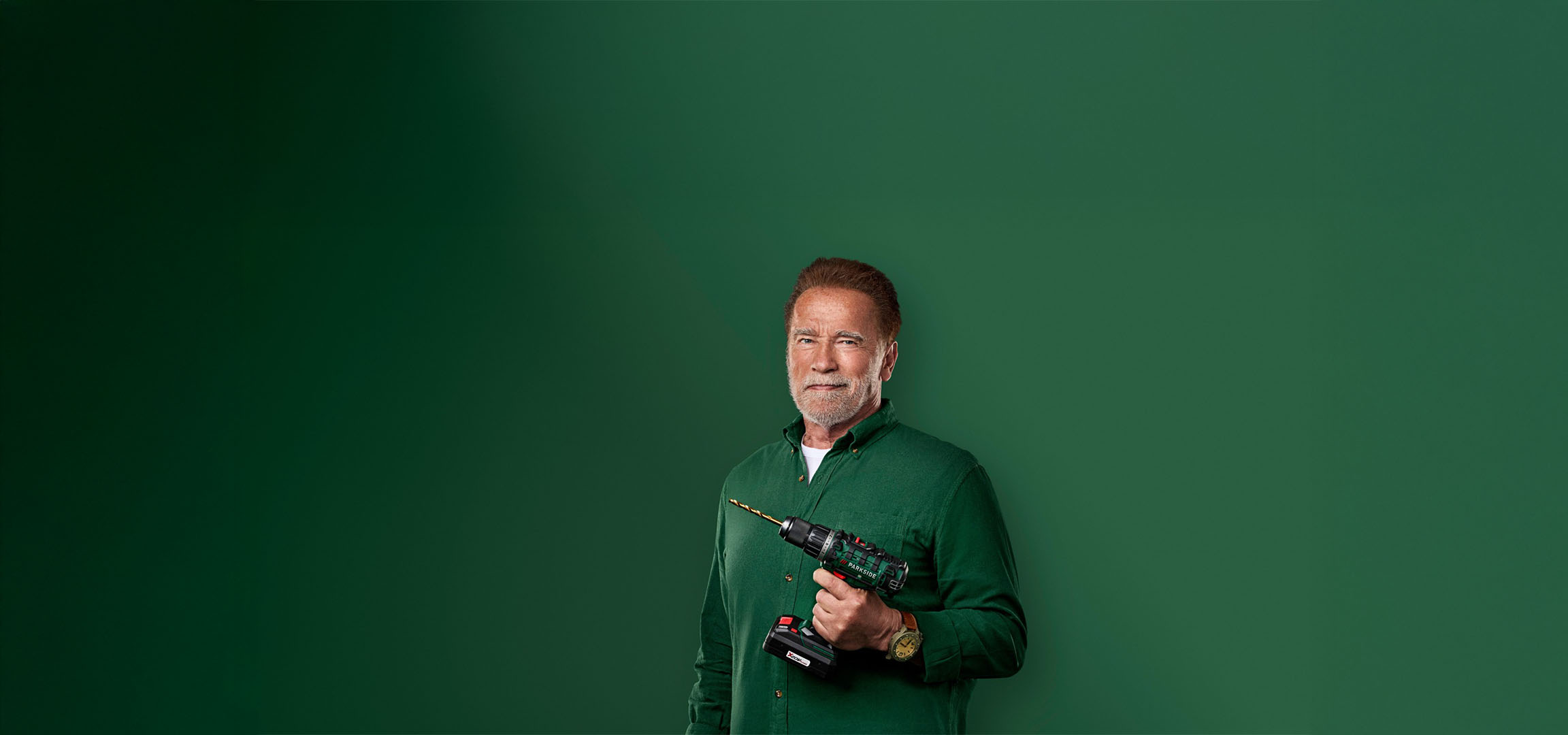 Arnold Schwarzenegger segurando uma furadeira Parkside em um fundo verde.