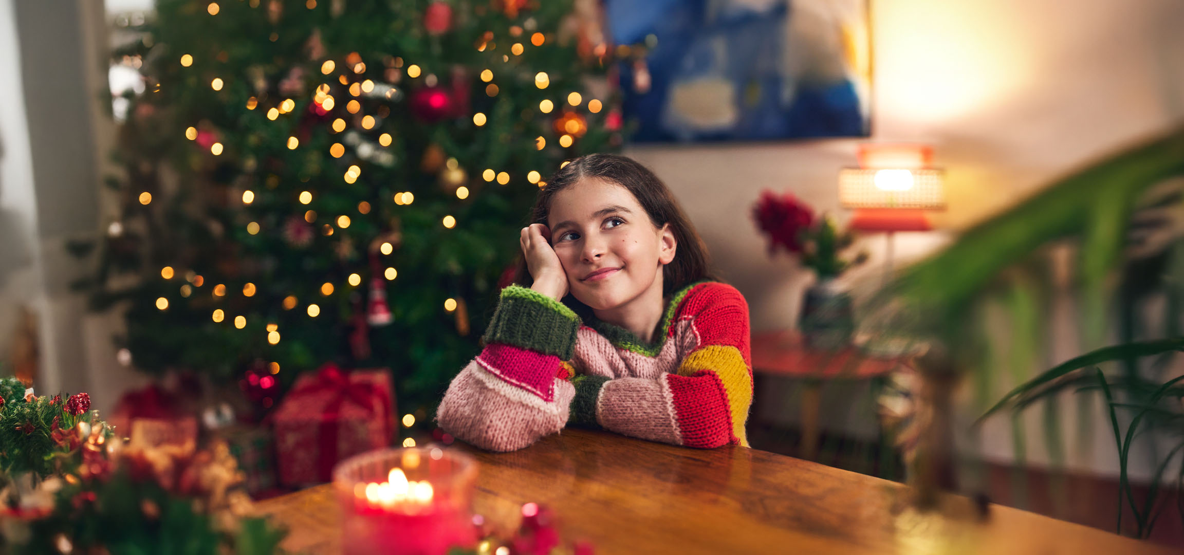 Menina sonhando durante o Natal, com uma árvore de Natal e presentes ao fundo.