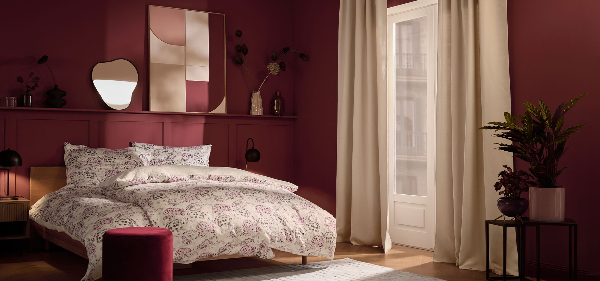 Quarto com paredes cor de vinho, cama com roupa de cama branca com estampa floral e plantas.