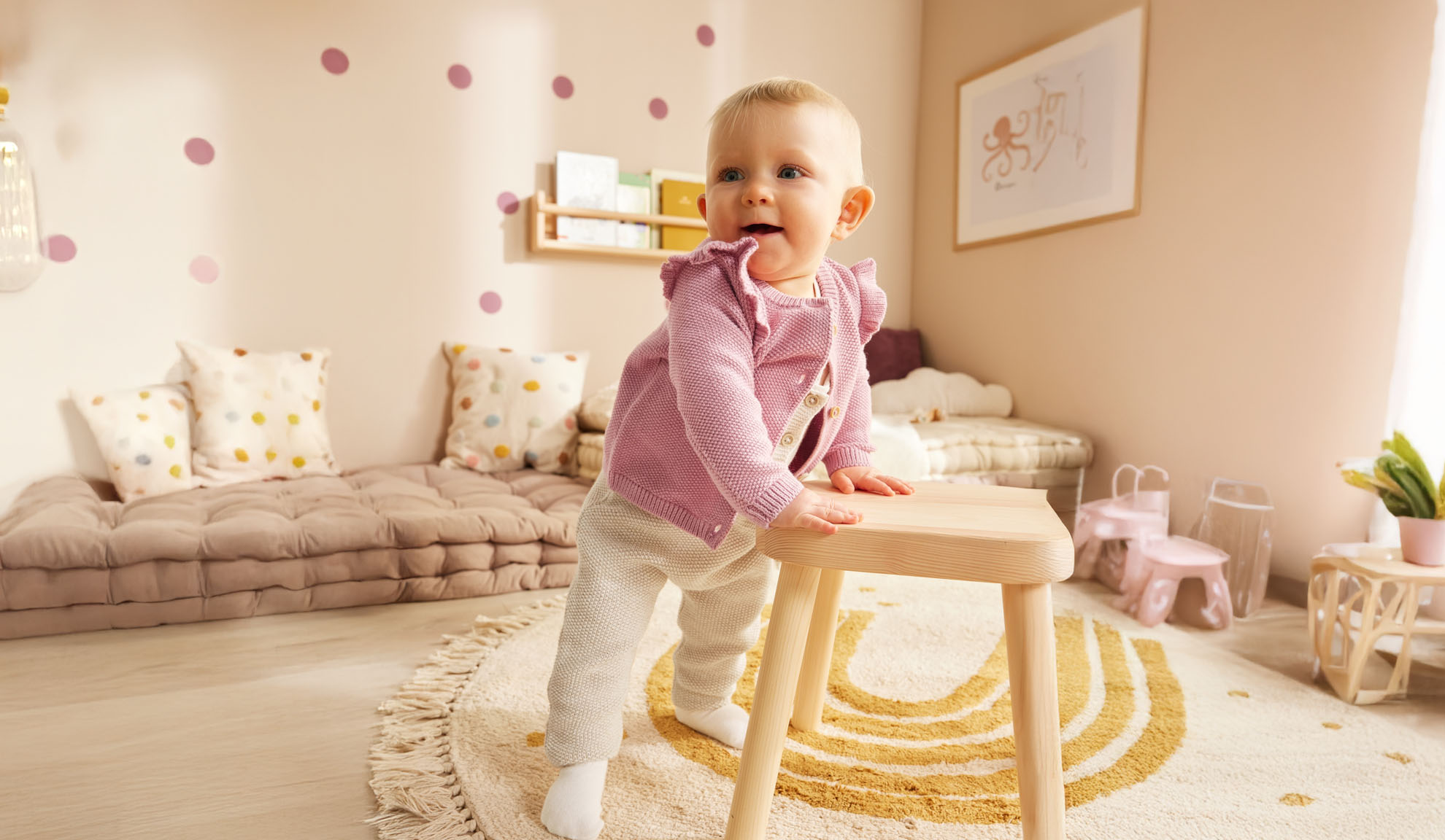 Uma criança pequena em pé perto de um banquinho de madeira em um quarto infantil decorado de forma minimalista.