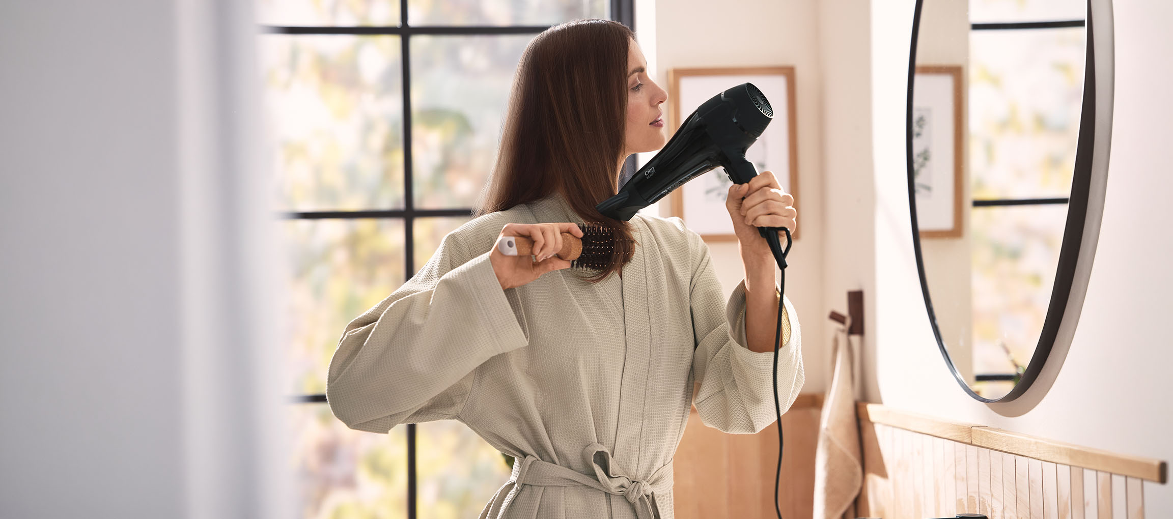 Mulher a secar o cabelo com um secador e uma escova na casa de banho.