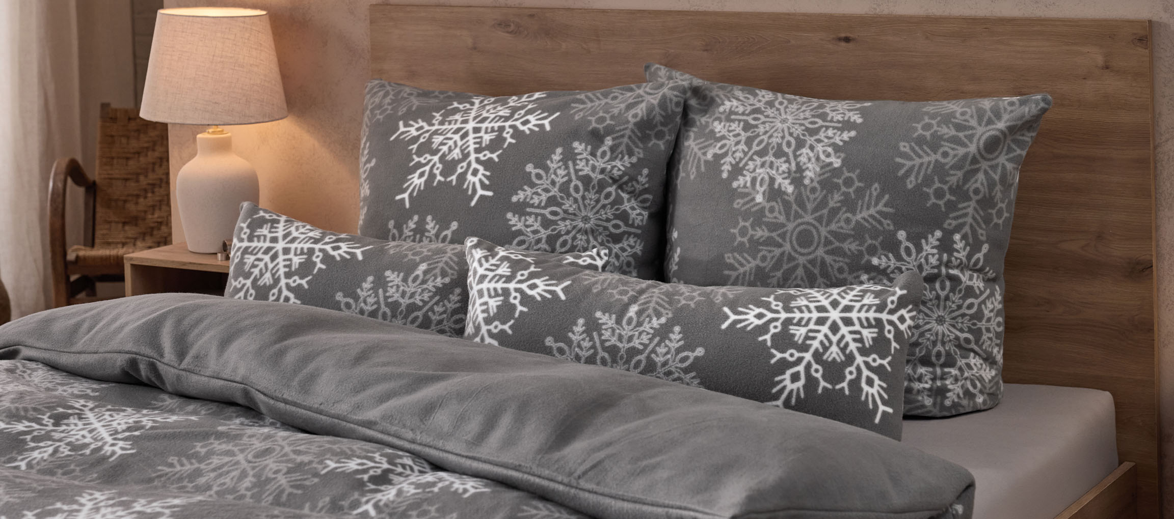 Roupa de cama cinzenta com padrão de flocos de neve e almofadas a condizer num quarto acolhedor.