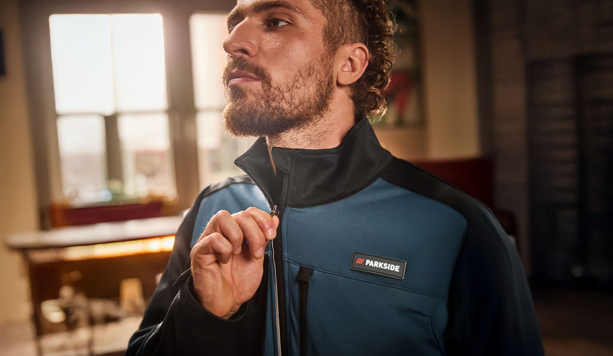 Homem com um casaco de trabalho Parkside azul e preto, a fechar o fecho.