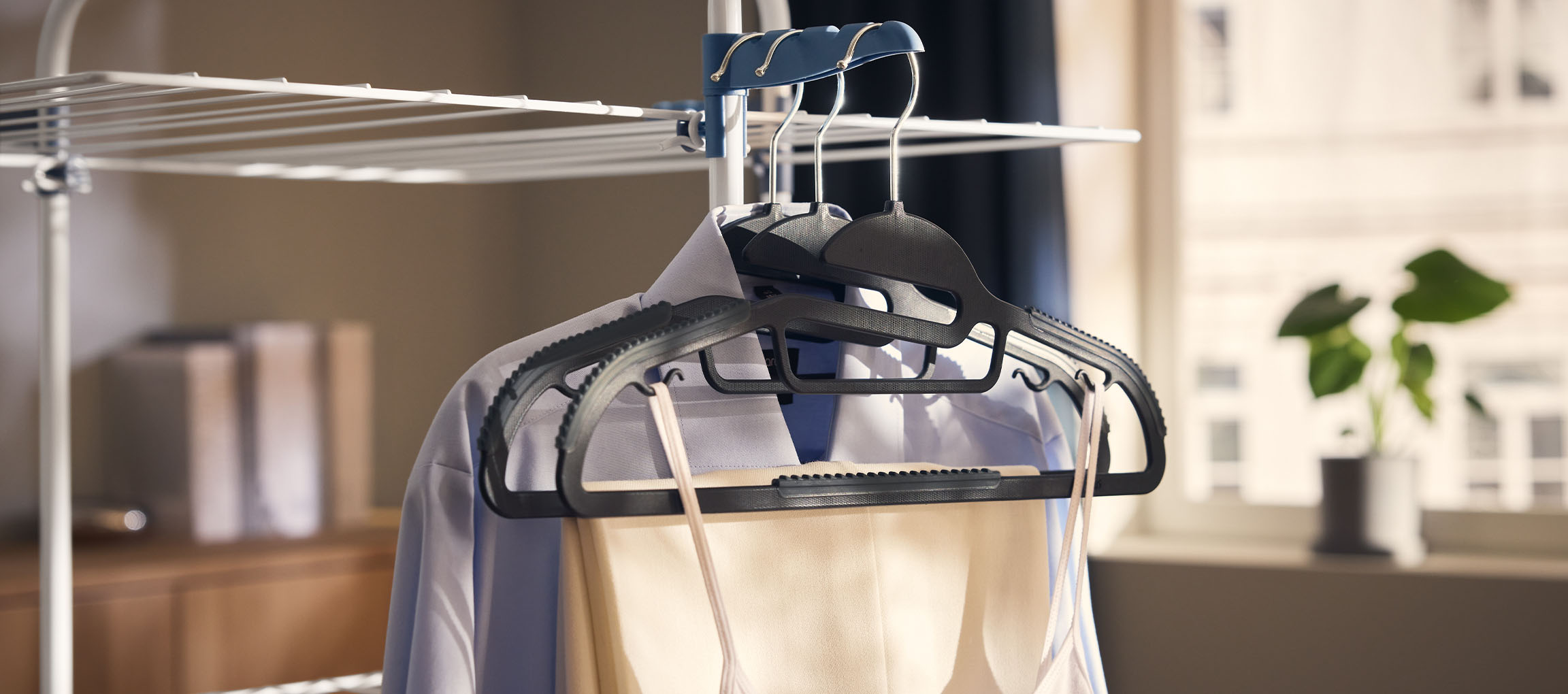 Roupa em cabides num estendal, com uma planta ao fundo.