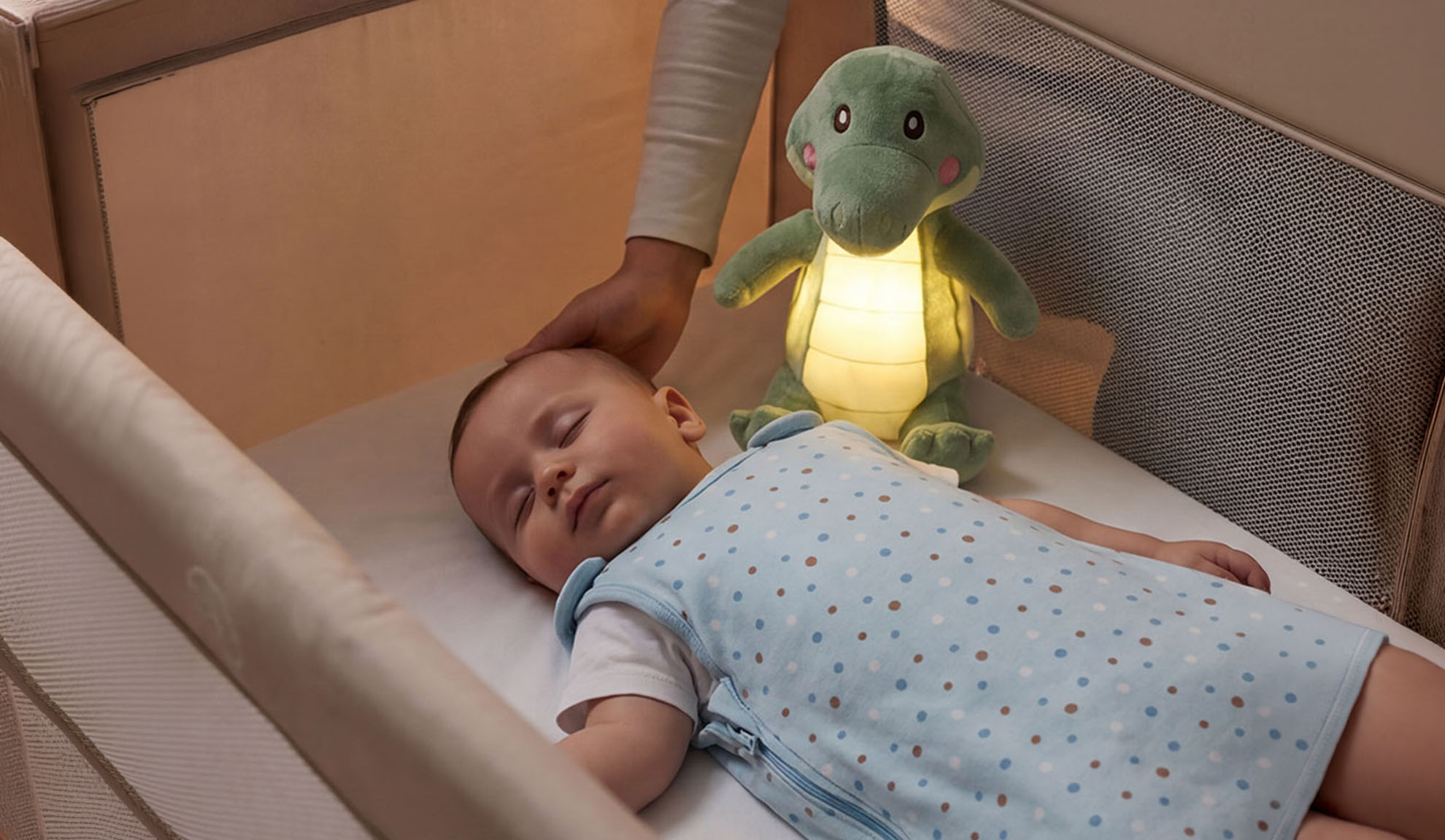Bebé a dormir num berço com um brinquedo de pelúcia e a mão de um pai.