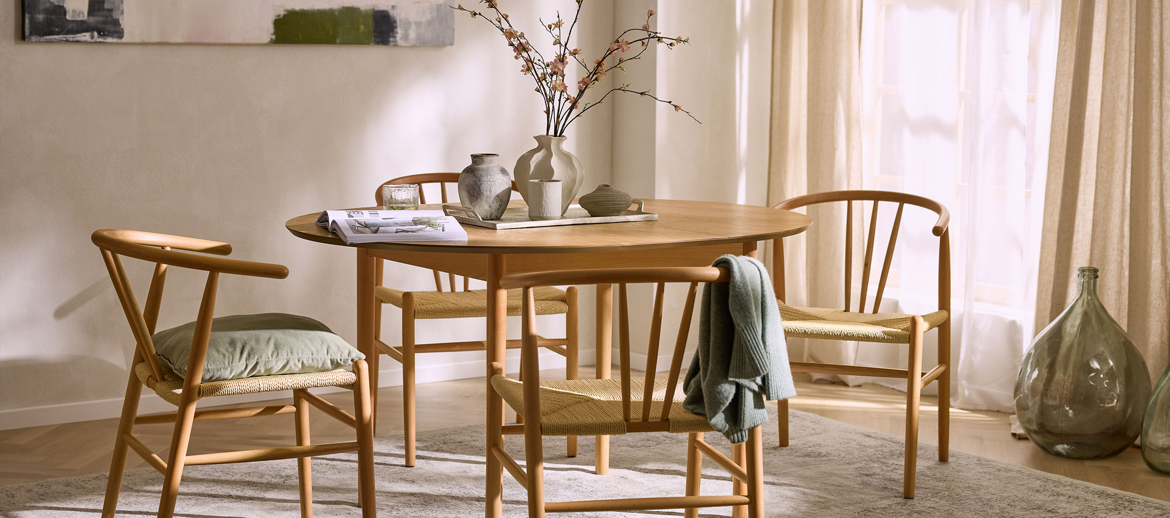 Sala de jantar com mesa redonda de madeira, cadeiras de madeira com assentos de corda e vasos decorativos.