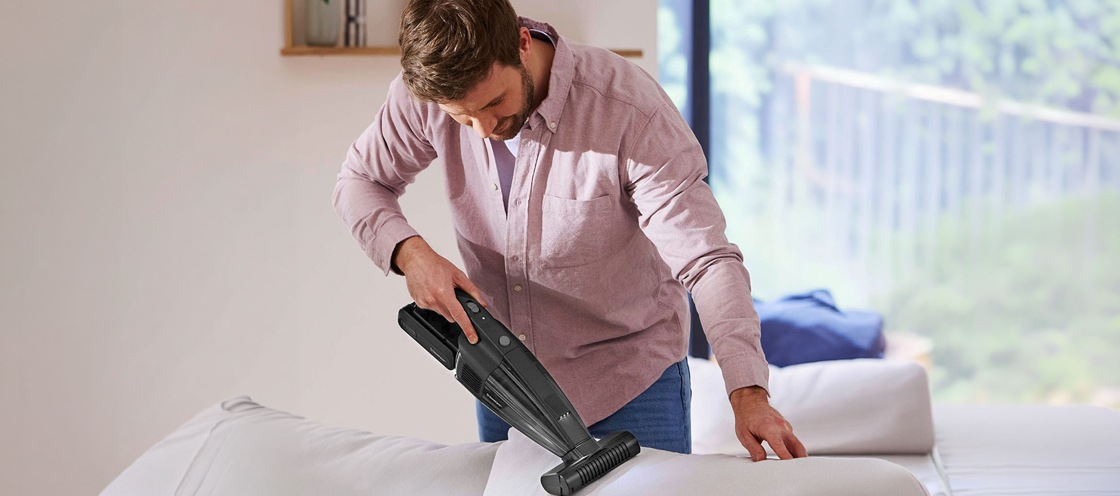 Homem a limpar um sofá com um aspirador de mão.