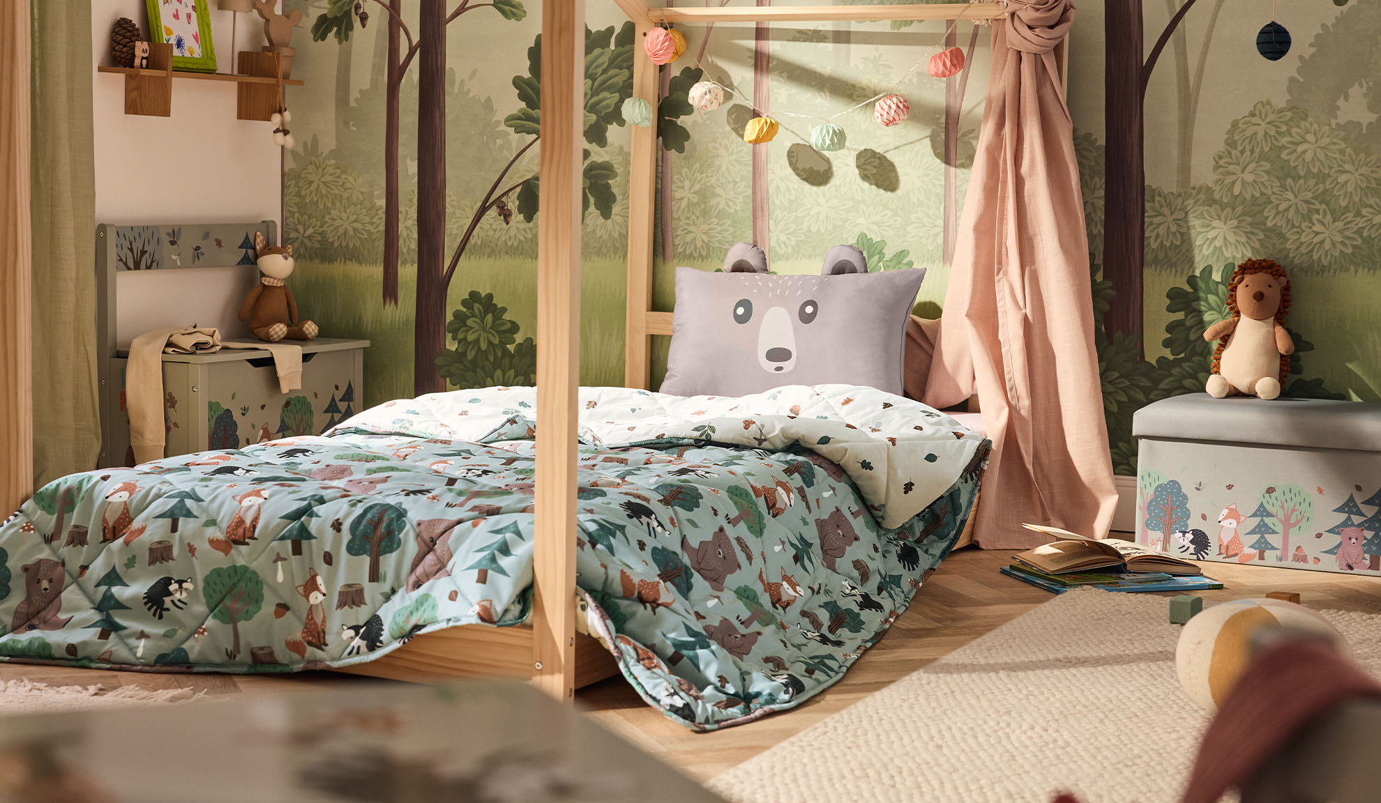 Quarto infantil com cama de madeira, almofada de urso e edredão com padrão florestal.