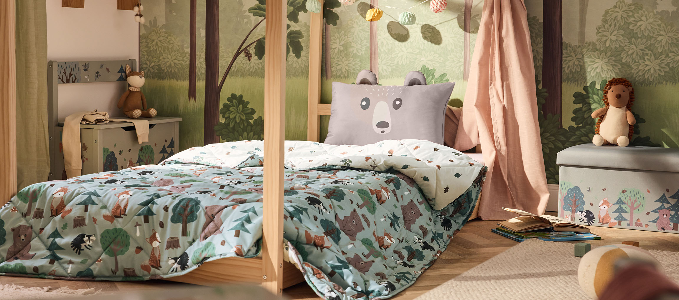 Quarto infantil com cama de madeira, almofada de urso e edredão com padrão florestal.