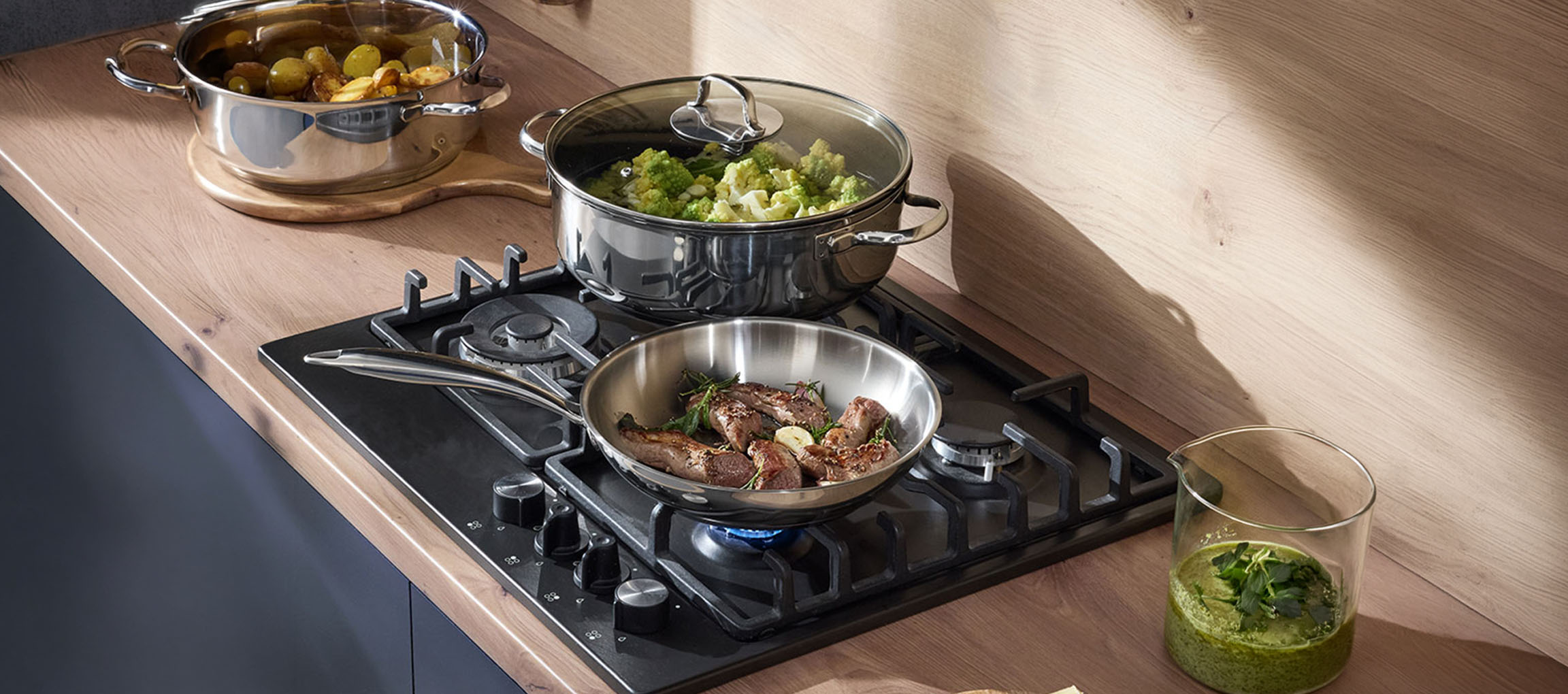 Placa a gás com panelas e frigideiras de aço inoxidável cheias de vegetais e carne.