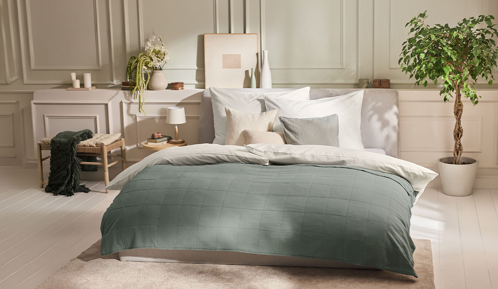Quarto com cama, capa de edredão verde, almofadas brancas e uma planta
