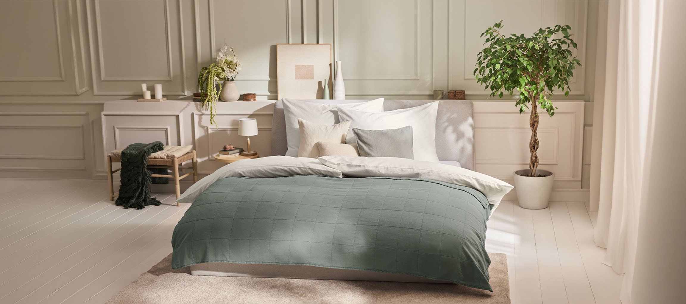 Quarto com cama, edredão verde, almofadas, mesa de cabeceira e uma planta.