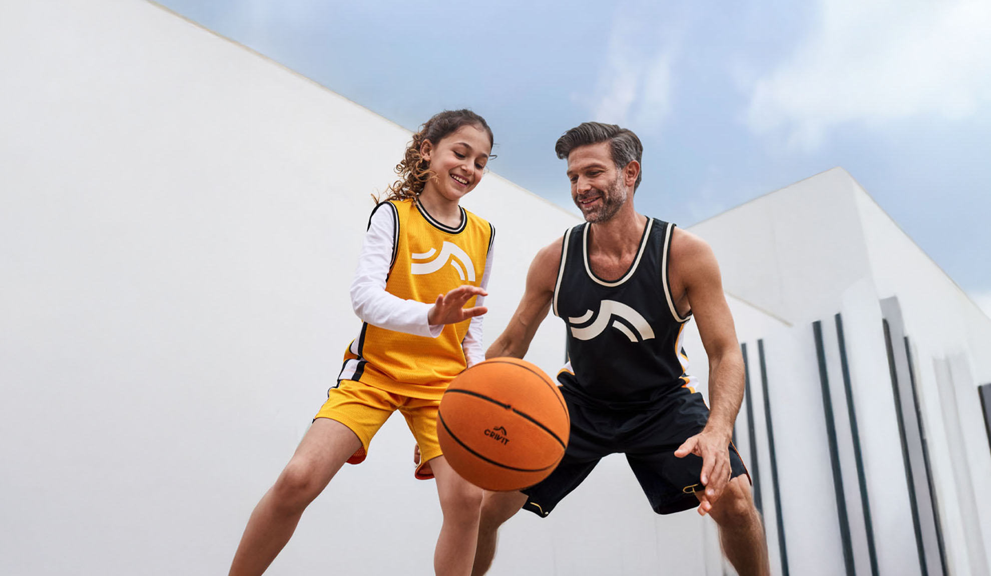 Pai e filha a jogar basquetebol com camisolas e calções Crivit.