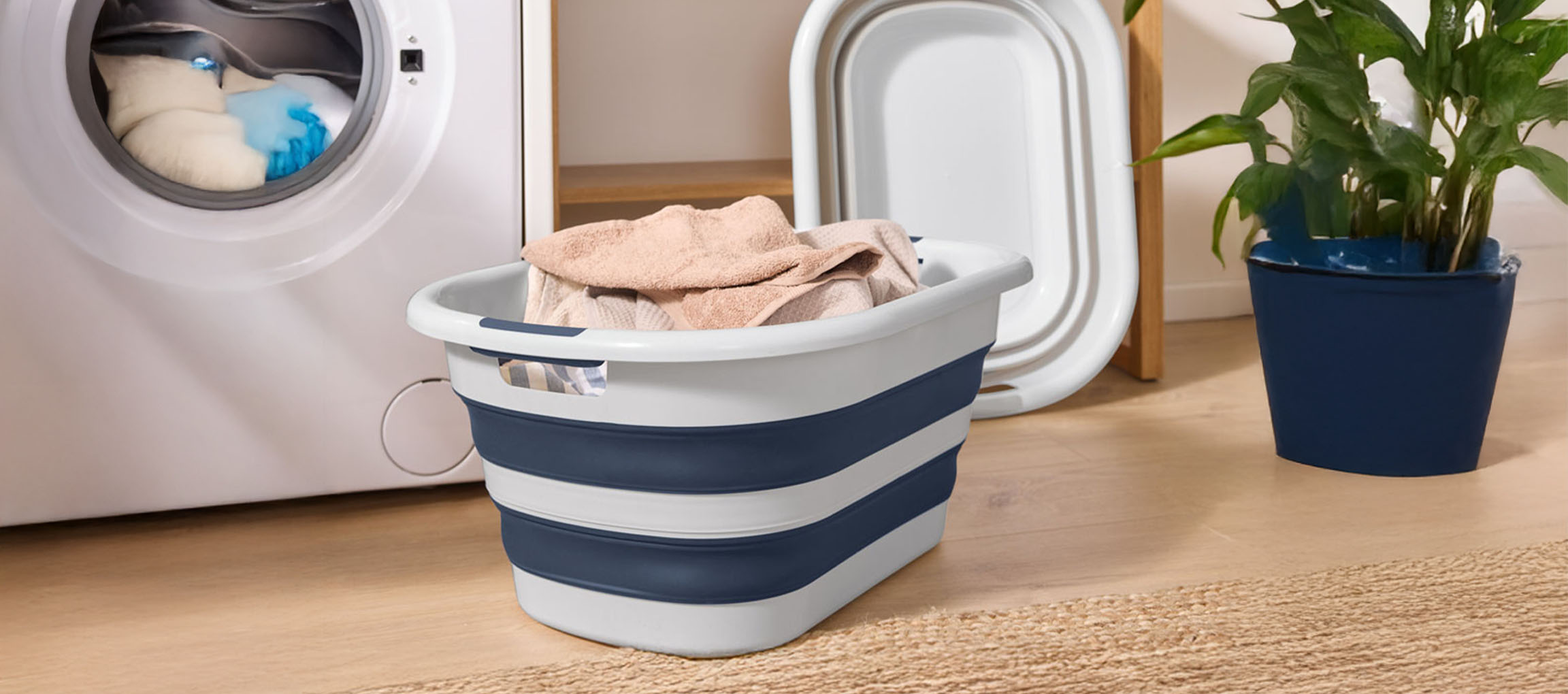 Uma máquina de lavar branca com um cesto de roupa dobrável azul e branco cheio de toalhas.