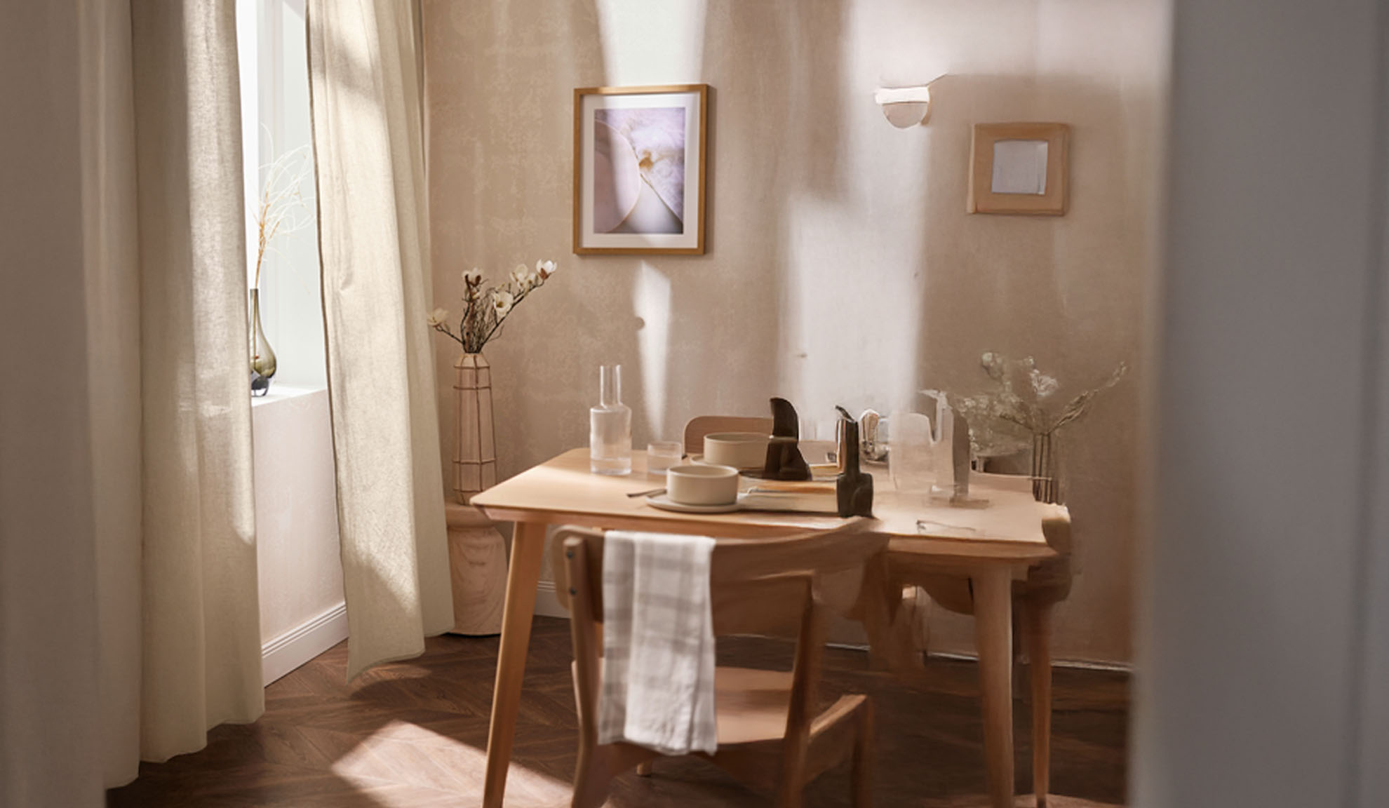 Uma sala de jantar com uma mesa de madeira posta para dois, com decoração clara e luz natural.