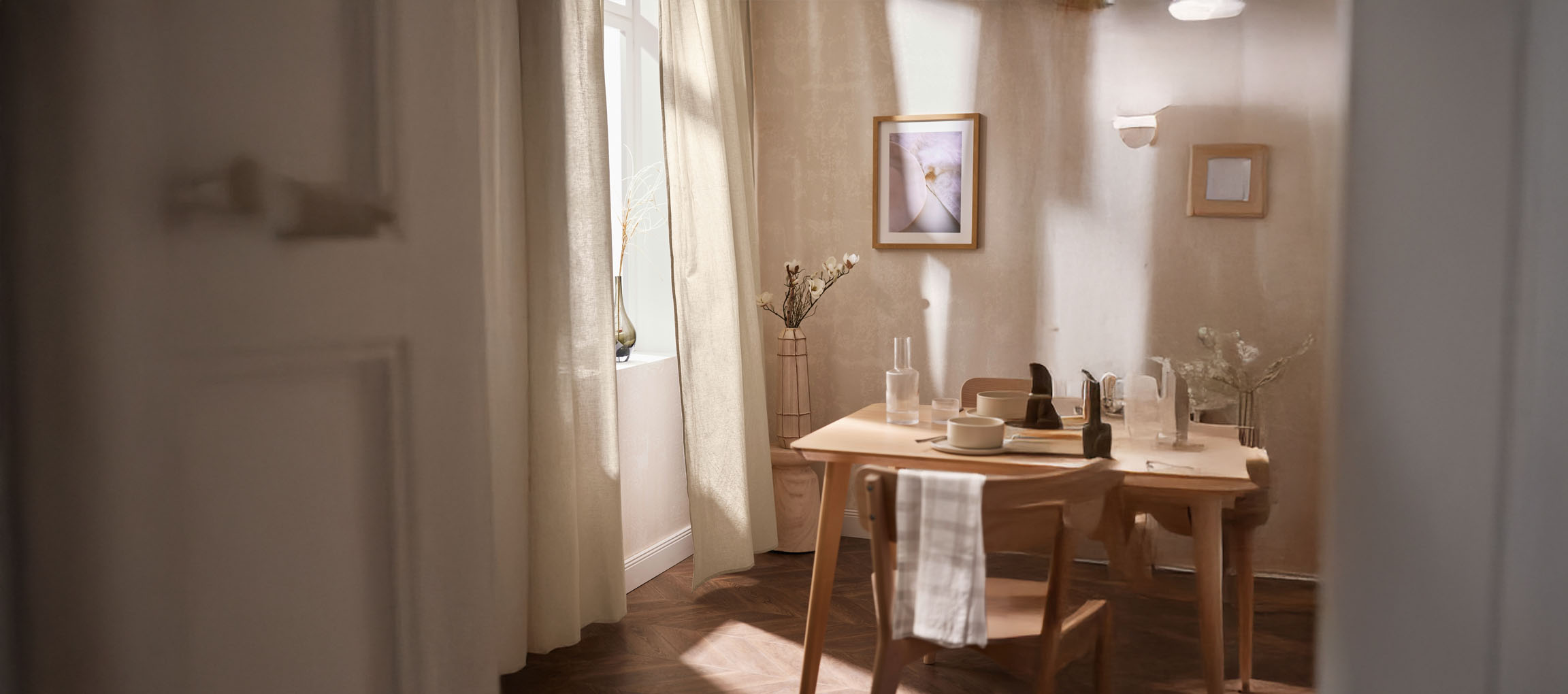 Sala de jantar iluminada com mesa de madeira, cadeiras e decorações minimalistas.