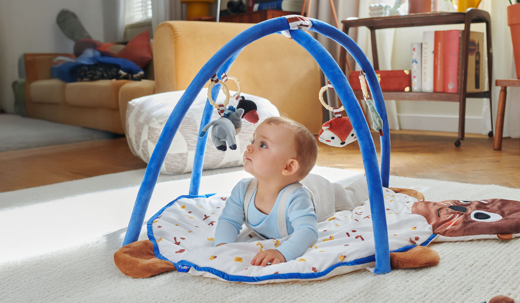 Um bebê brinca em um tapete de atividades Tiny Love com um arco em forma de animais.