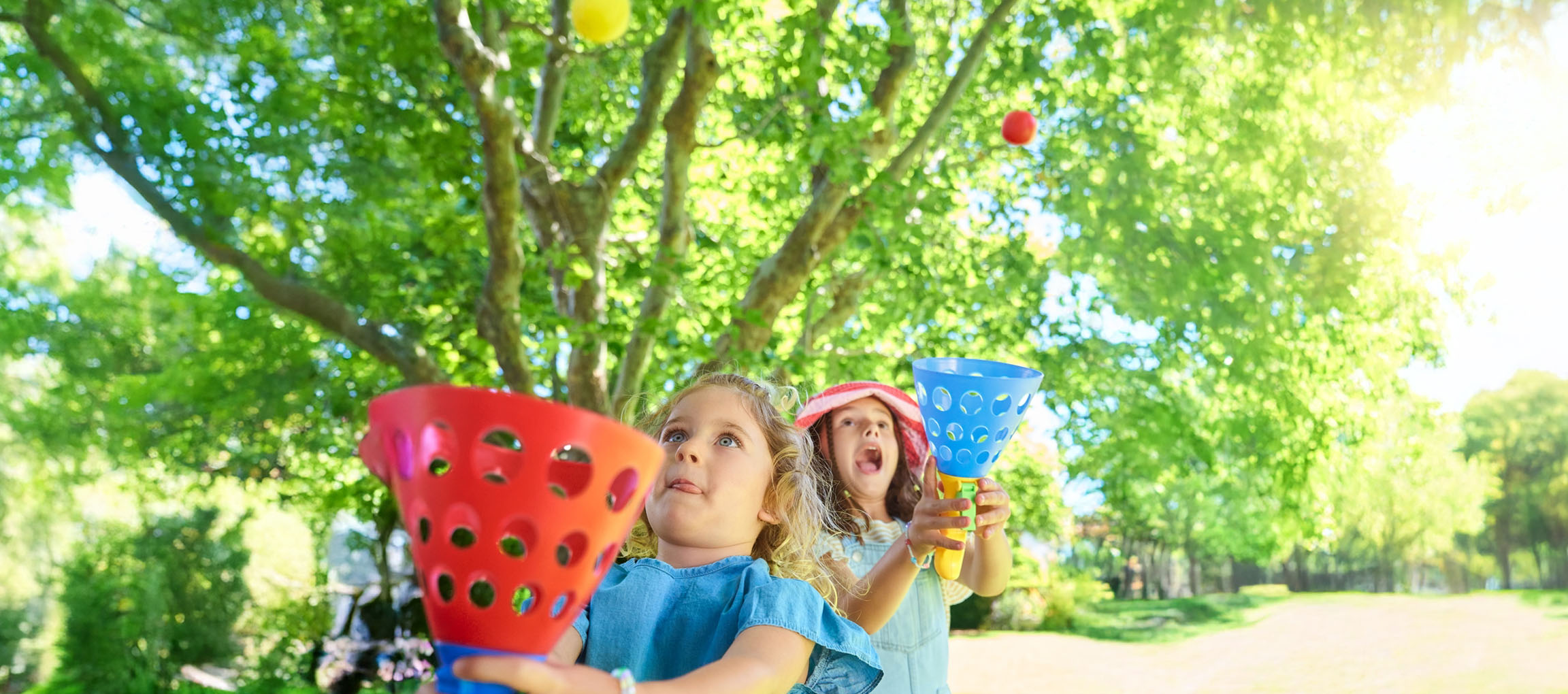 Duas meninas brincam com bolas coloridas em um parque ensolarado.