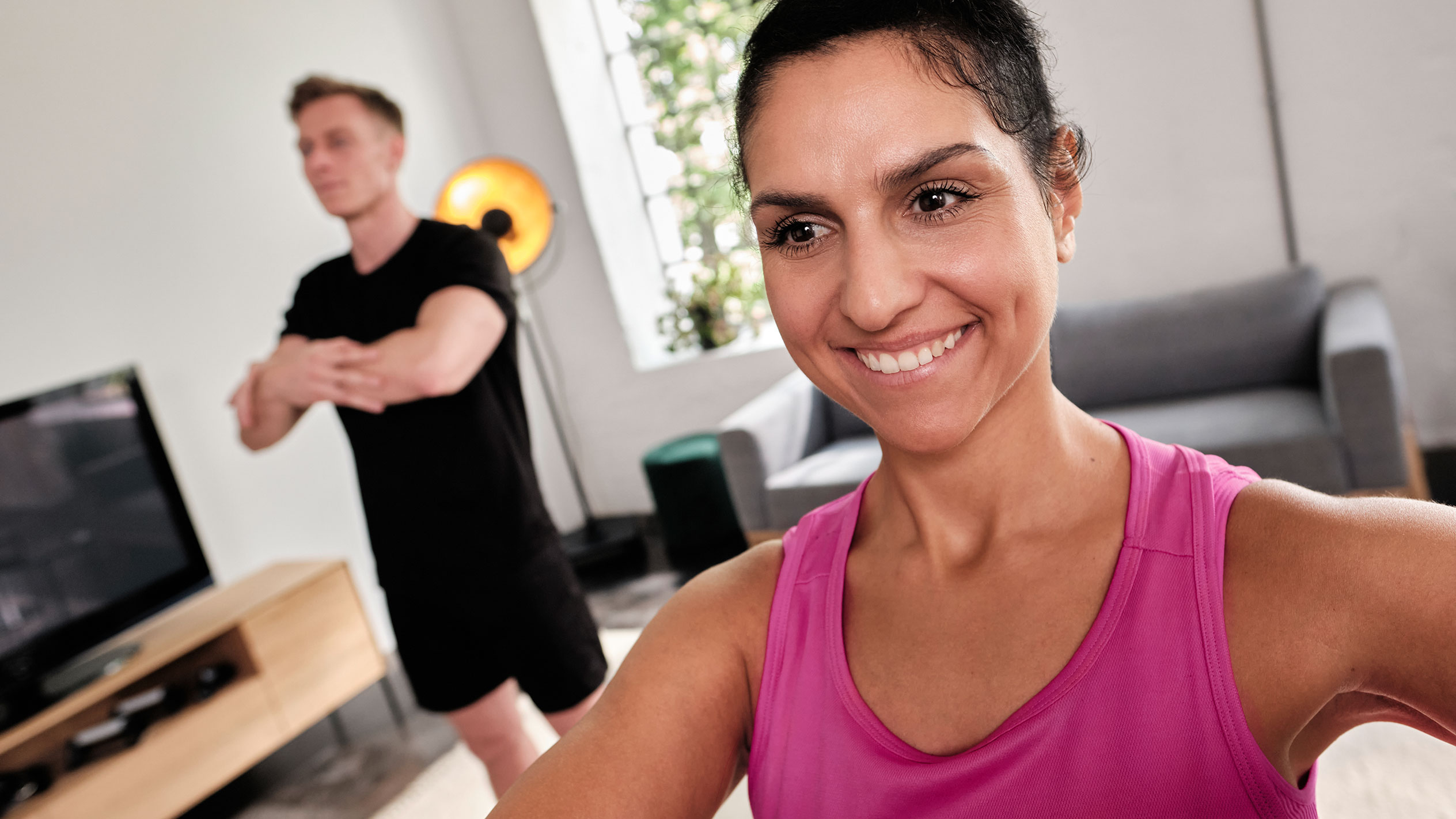 Mulher sorridente se exercitando em casa com seu parceiro.