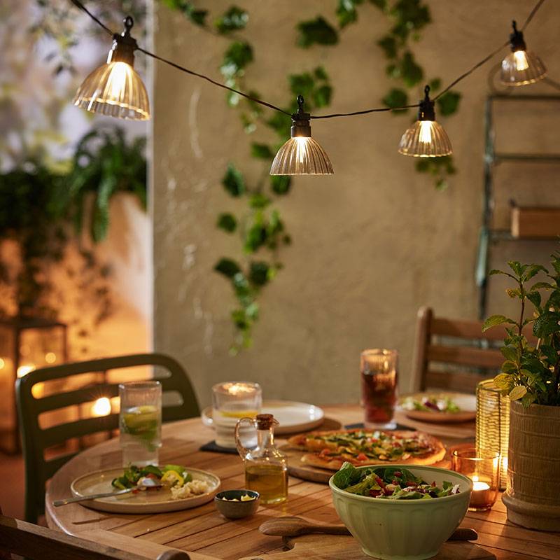 Iluminação externa com luzes quentes sobre uma mesa de madeira com comida.