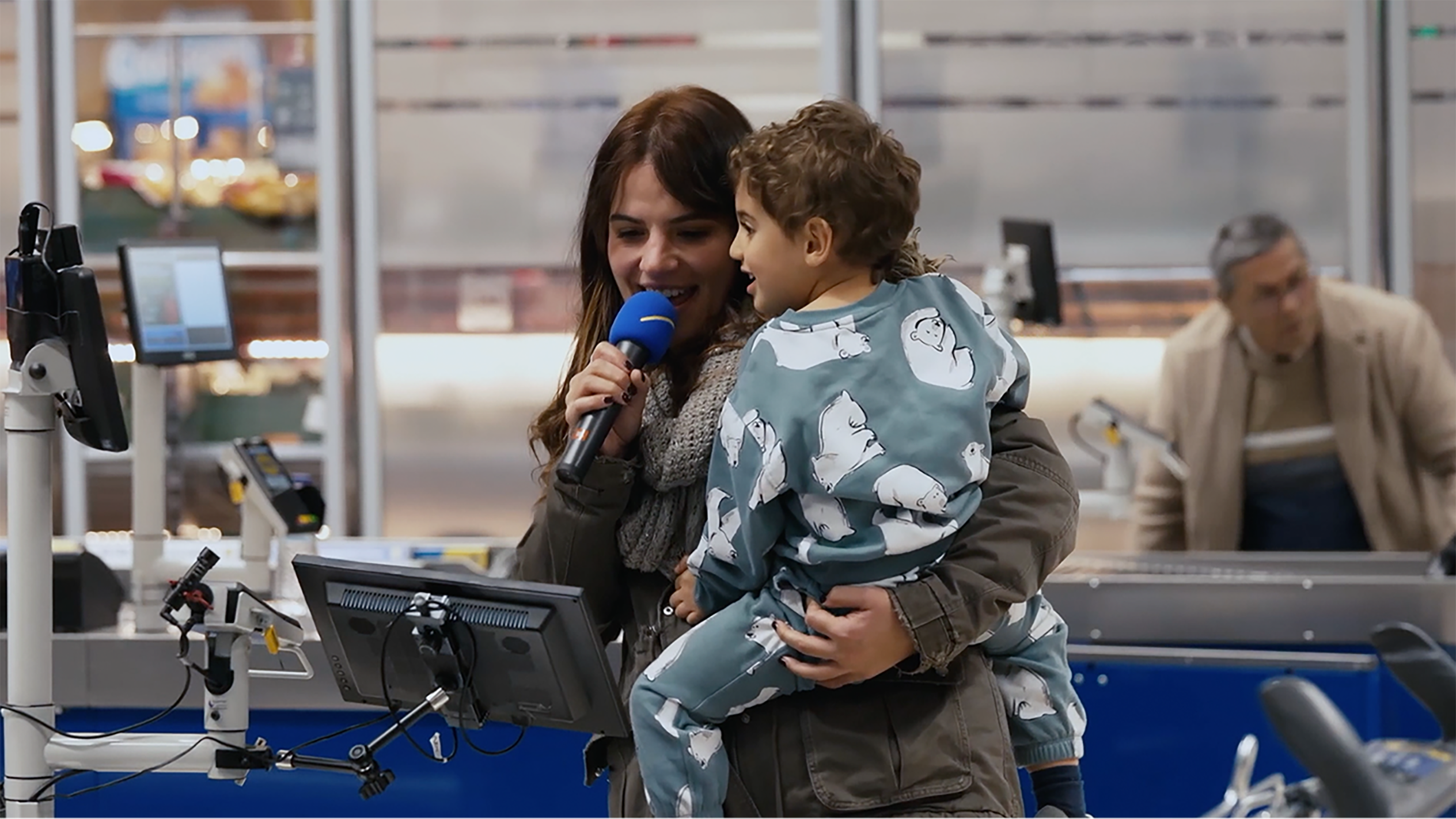 Mulher e criança cantam num microfone num supermercado Lidl.
