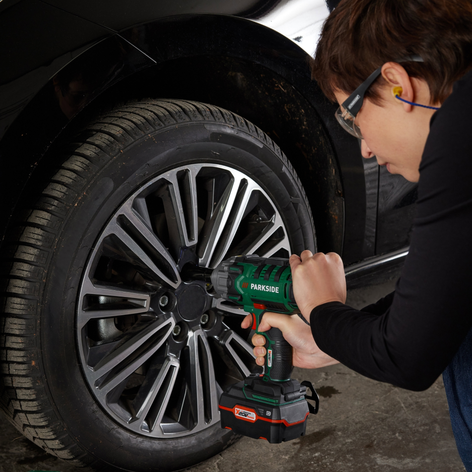 Uma pessoa usa uma chave de impacto sem fio para apertar os parafusos de uma roda de carro.
