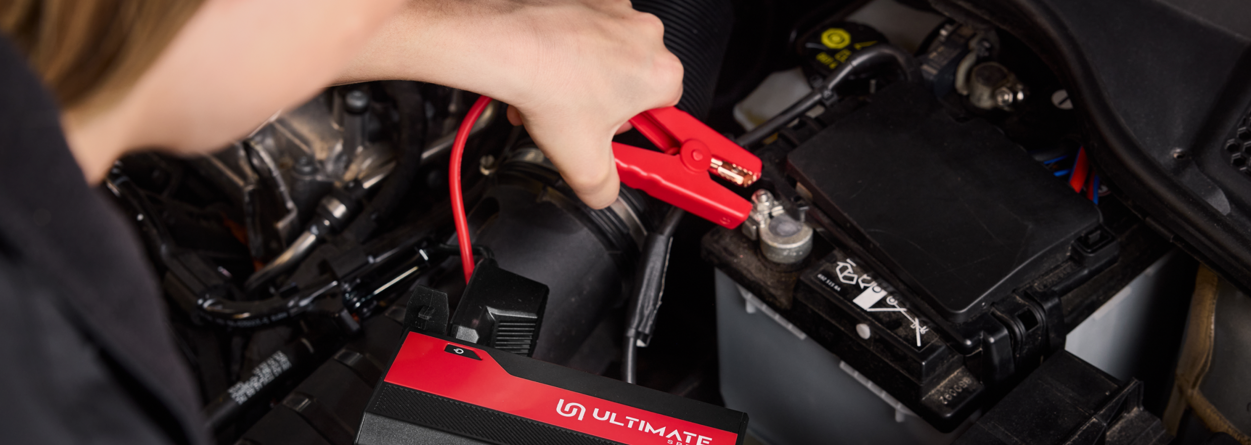 Pessoa a ligar um carregador de bateria Ultimate Speed a uma bateria de carro.