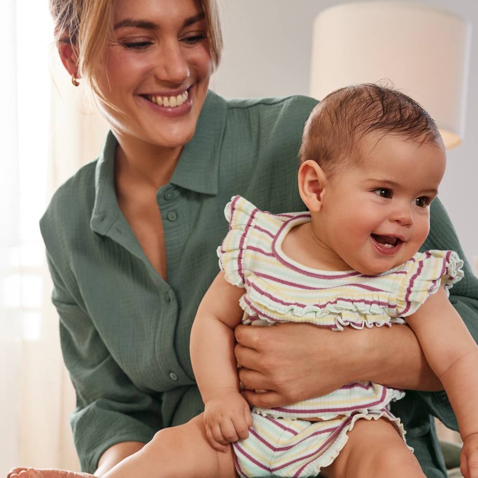 Mãe sorridente com um bebé feliz a usar um conjunto às riscas coloridas.