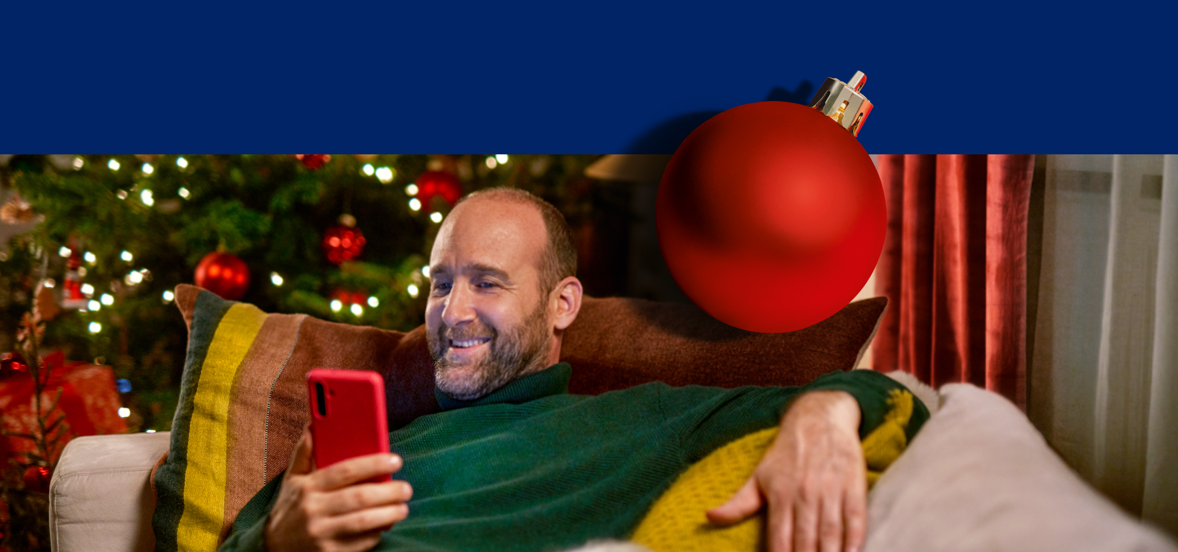 Homem sorridente a usar um smartphone no sofá, com uma árvore de Natal e um logótipo Lidl Plus.