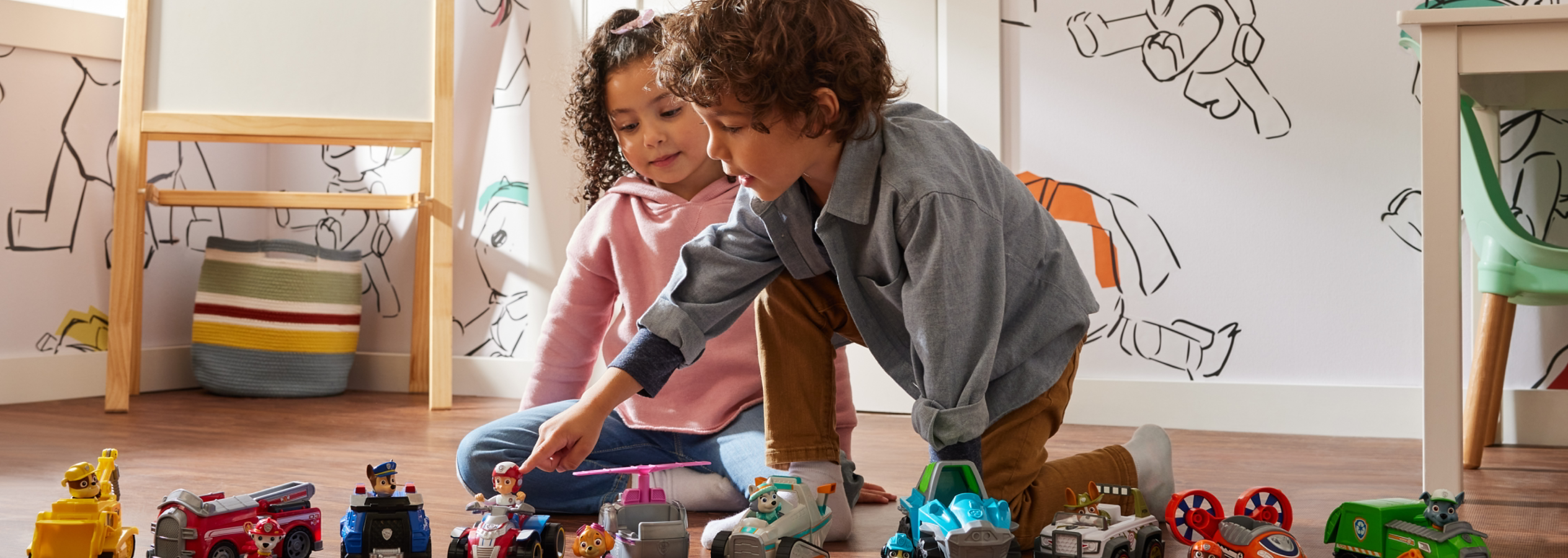 Duas crianças a brincar no chão com brinquedos da Patrulha Pata.