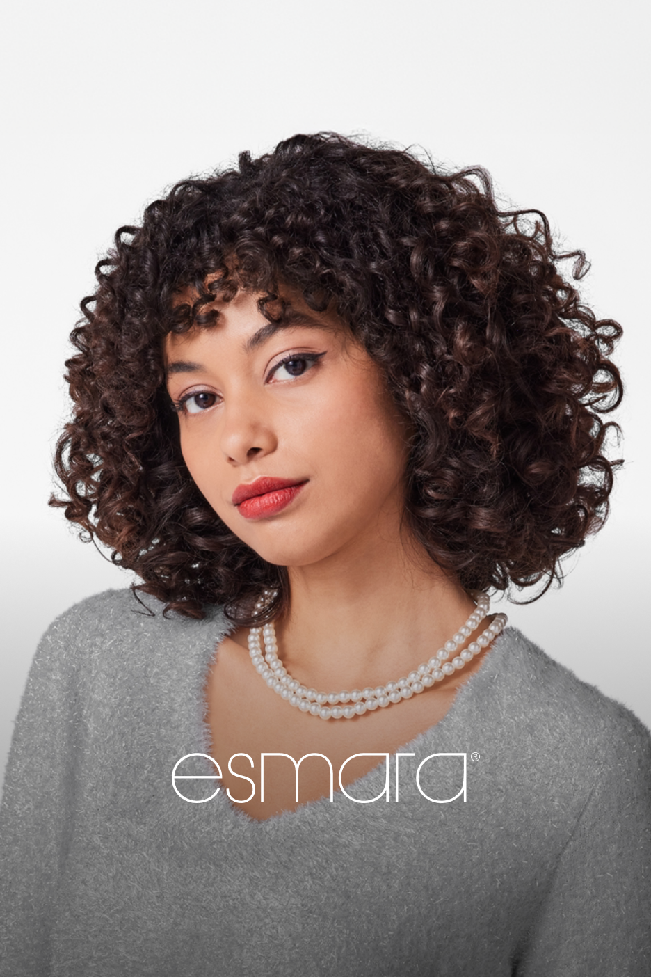 Mulher com cabelo encaracolado, camisola cinzenta e colar de pérolas, marca Esmara.