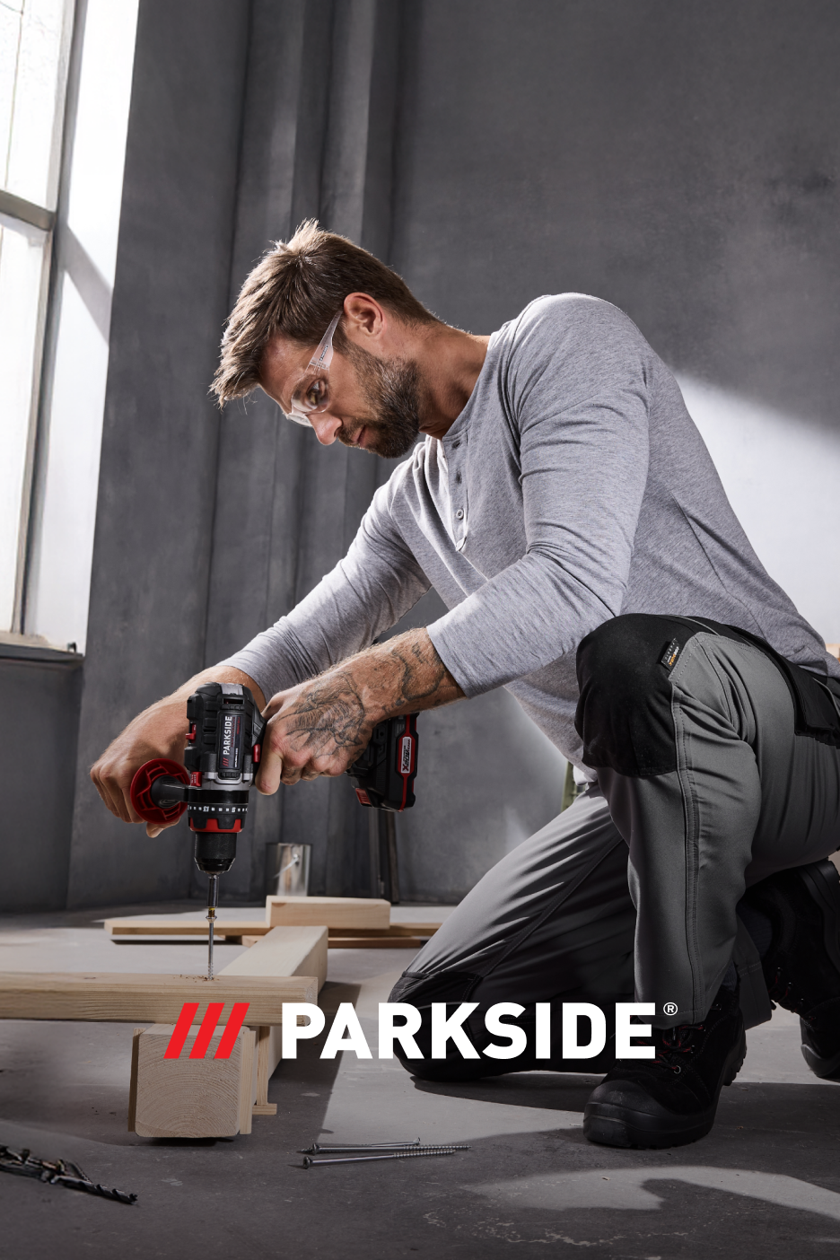 Homem a usar uma berbequim Parkside para perfurar madeira, com óculos de segurança.