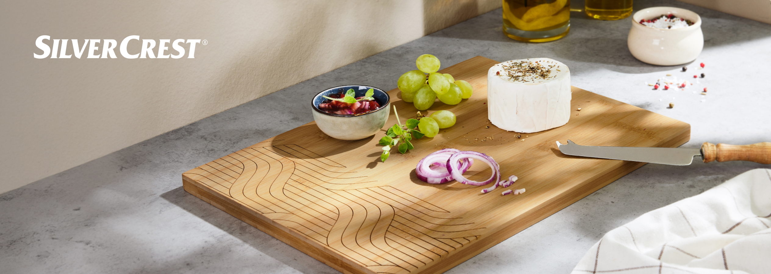 Tábua de bambu SilverCrest com queijo, uvas, cebola roxa e molho.