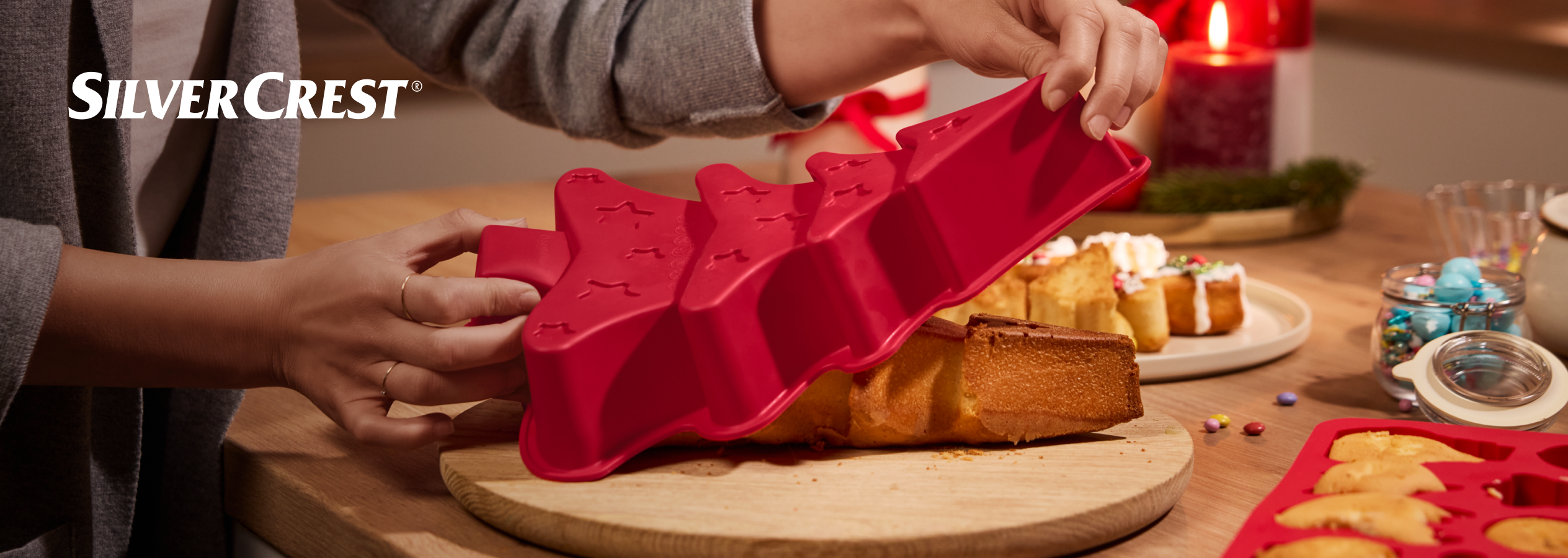 Mãos a desenformar um bolo em forma de árvore de Natal de uma forma de silicone SilverCrest.