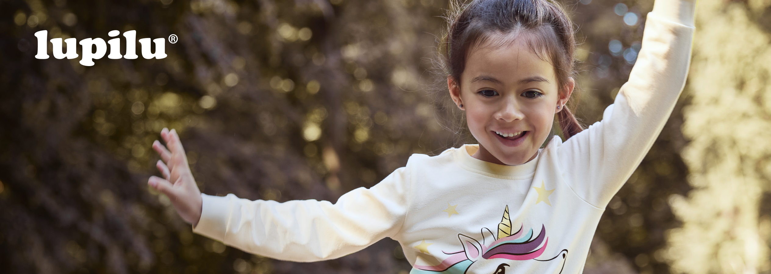 Menina sorridente com camisola de unicórnio Lupilu