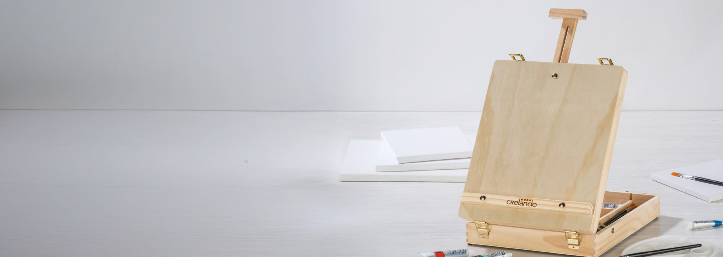 Cavalete de mesa de madeira Crelando com telas, tintas e pincéis.