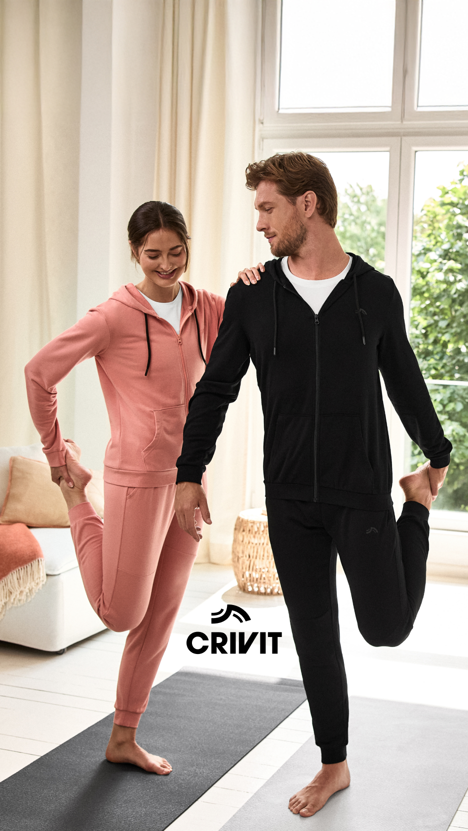 Um casal a alongar-se em fatos de treino Crivit, ele de preto e ela de rosa.