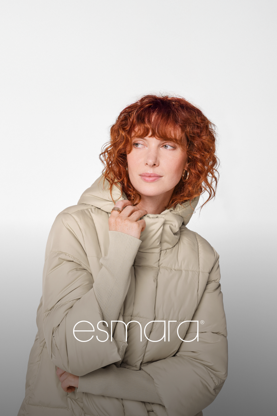 Mulher de cabelo ruivo encaracolado a usar um casaco acolchoado bege da Esmara.