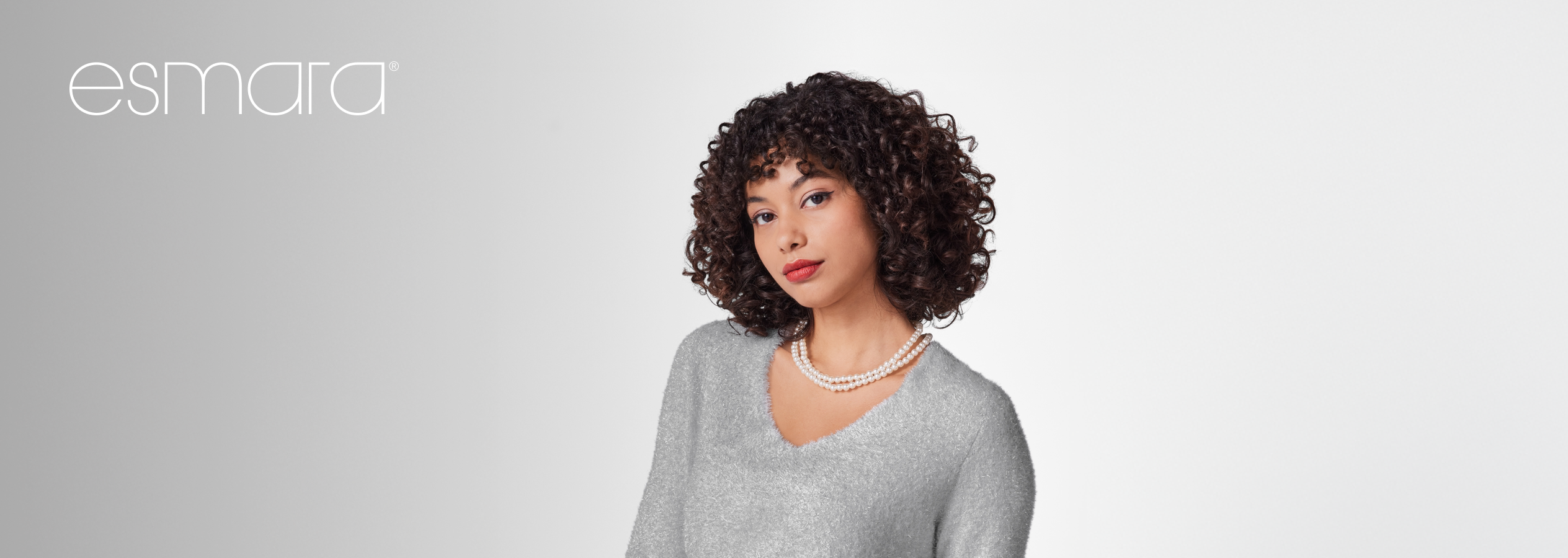 Mulher com cabelo encaracolado, camisola cinzenta Esmara e colar de pérolas.