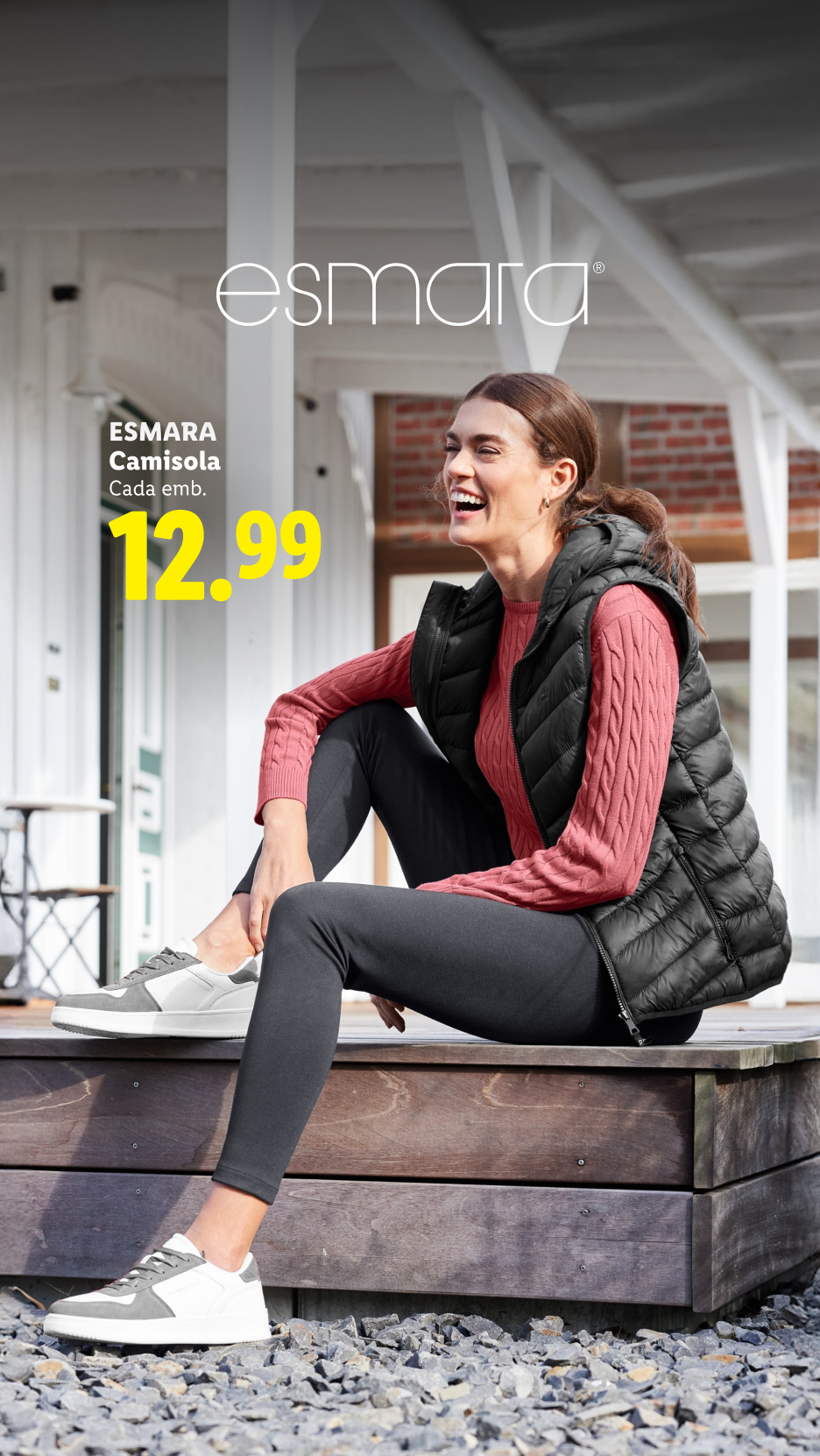 Mulher sorridente com colete acolchoado preto e camisola rosa, sentada ao ar livre. Preço: 12.99.