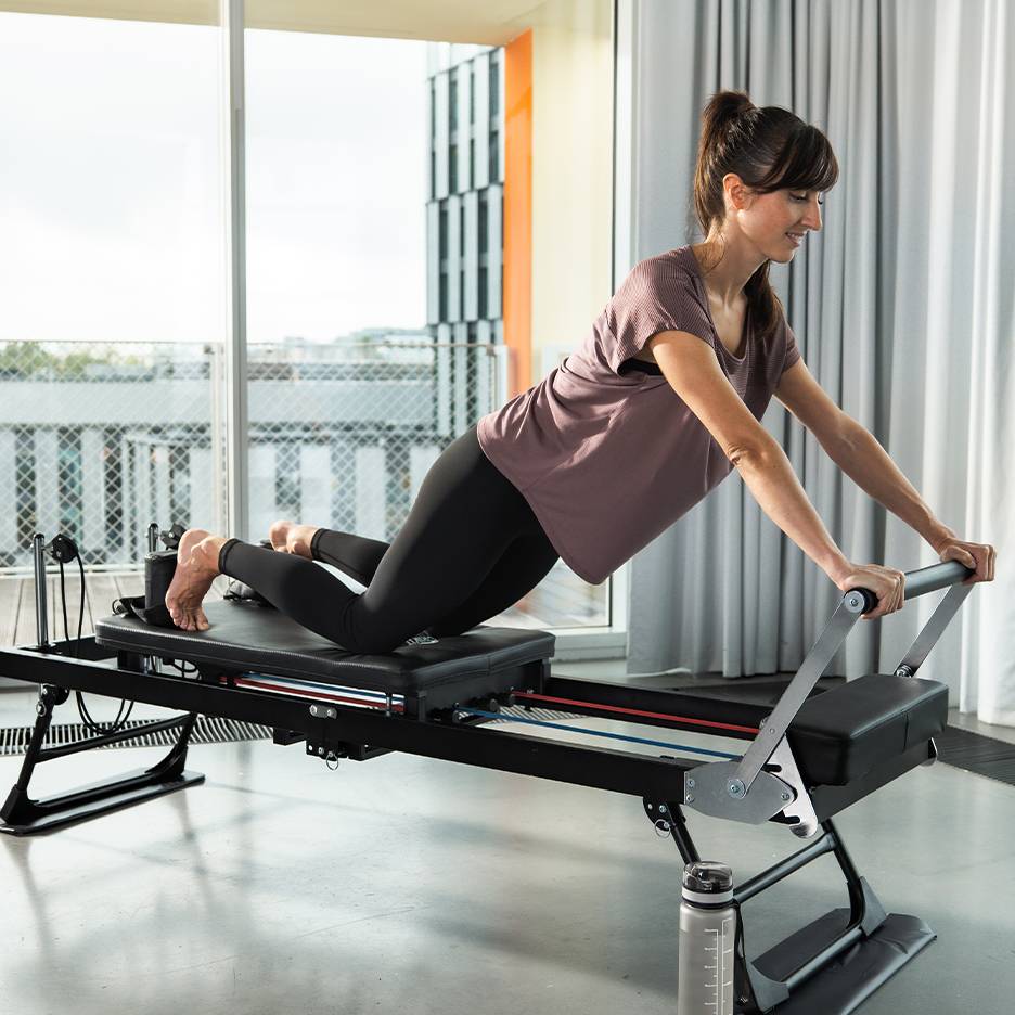 Mulher a fazer Pilates num reformer com molas e correias.