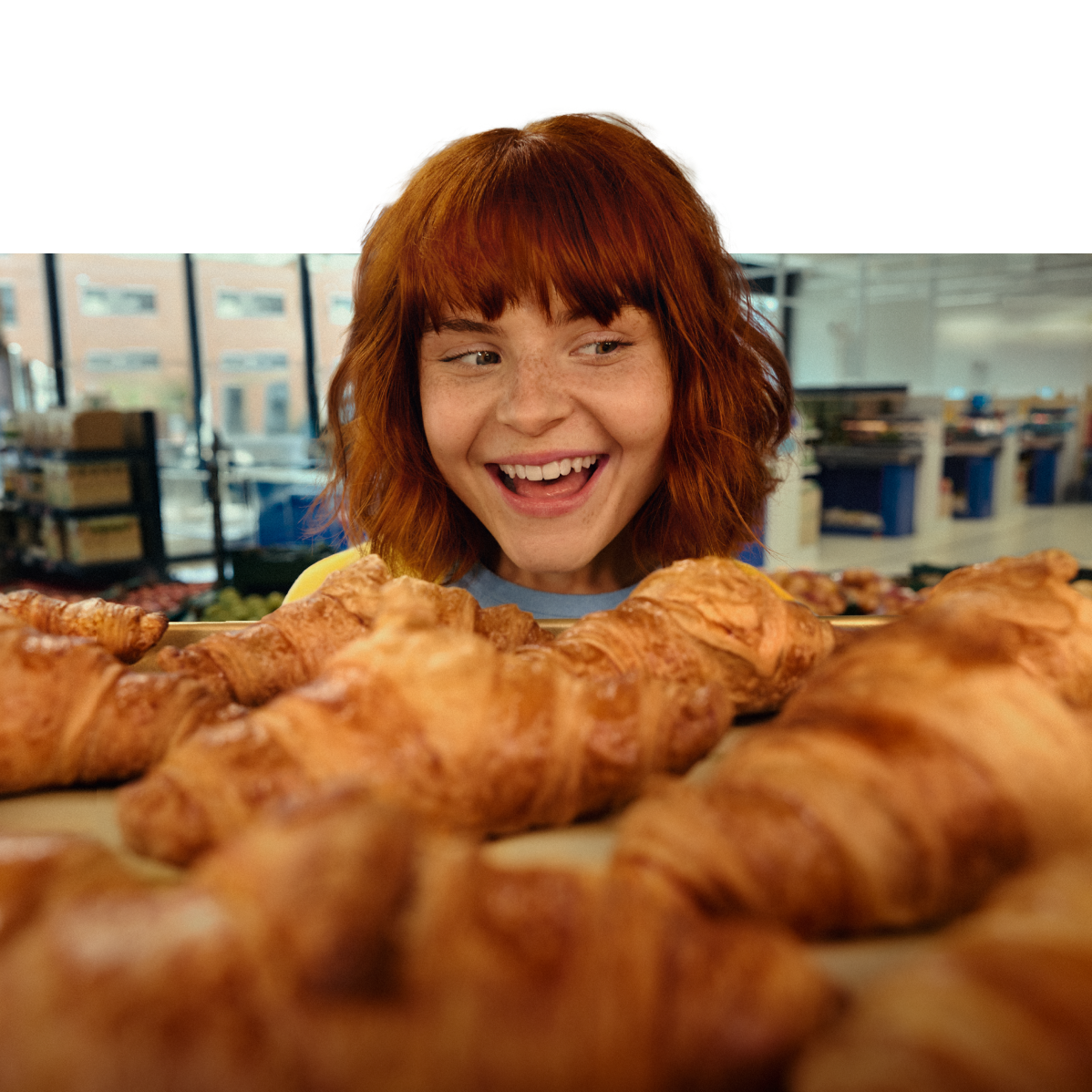 Mulher ruiva sorridente olhando para croissants frescos em uma padaria.