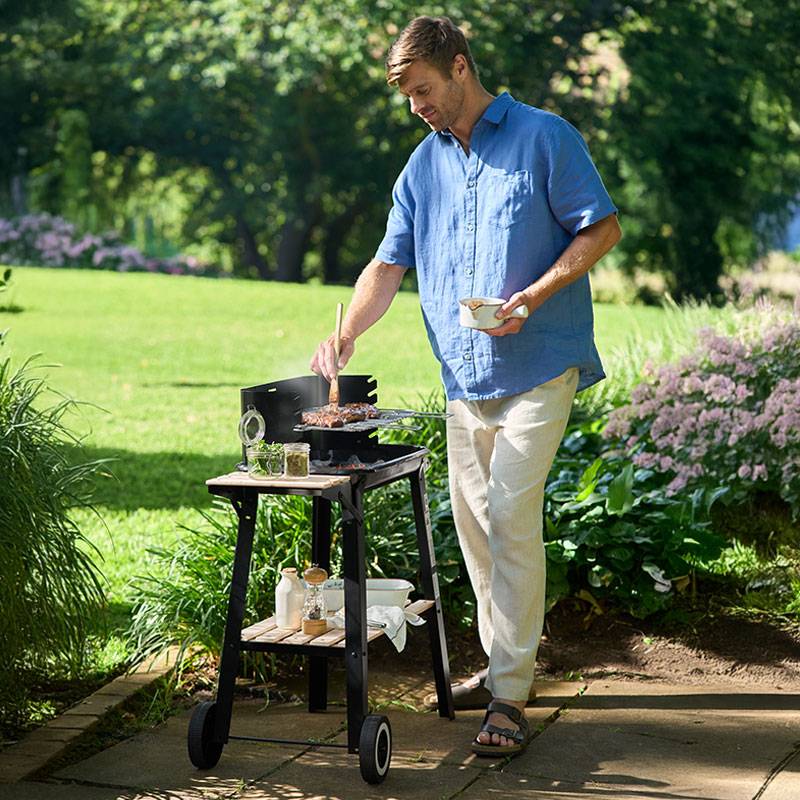 Homem grelhando bifes em um churrasco no jardim.