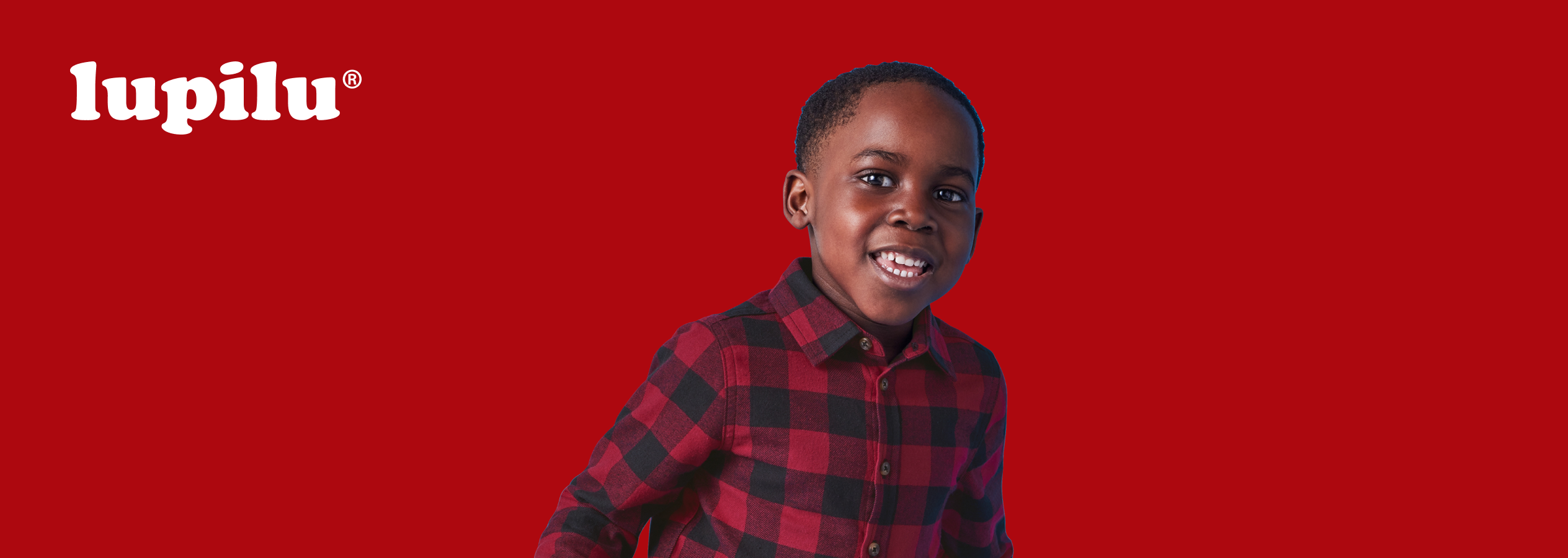 Lupilu: Um menino sorridente com camisa xadrez vermelha e preta.