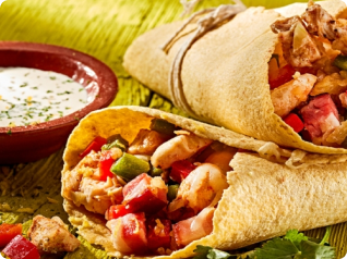 Dois wraps de tortilha recheados com carne e vegetais, com um molho cremoso ao lado.