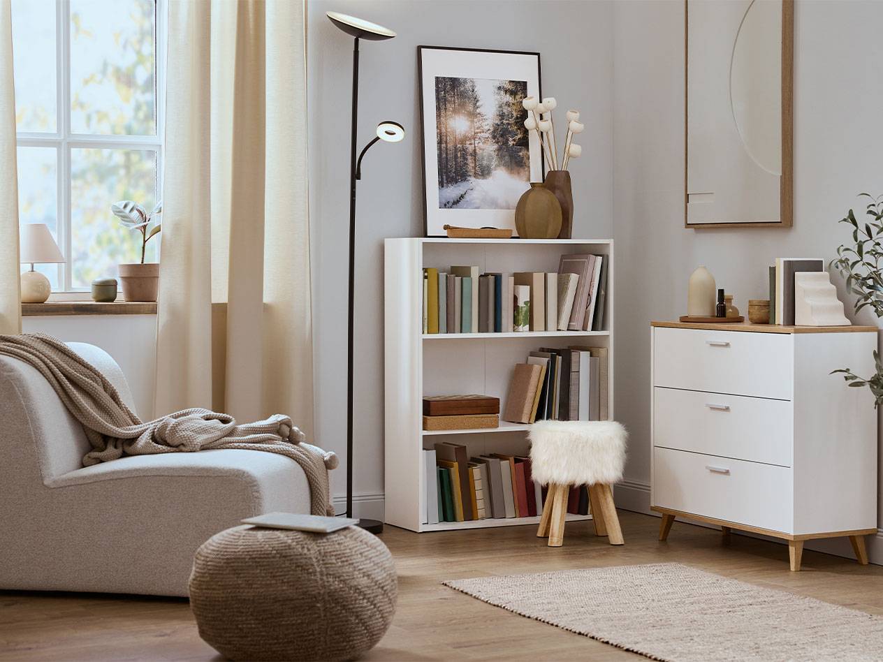 Sala de estar acolhedora com poltrona, estante e cómoda em tons neutros.