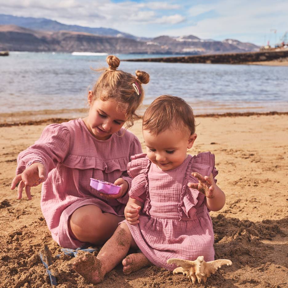 Duas meninas com vestidos rosa a brincar na areia da praia.