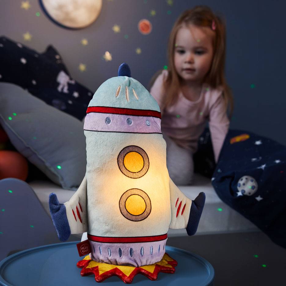 Menina olha para um candeeiro de noite em forma de foguetão num quarto temático espacial.